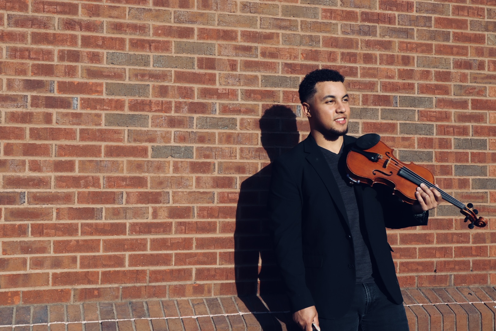 Ian holding violin against brick wall